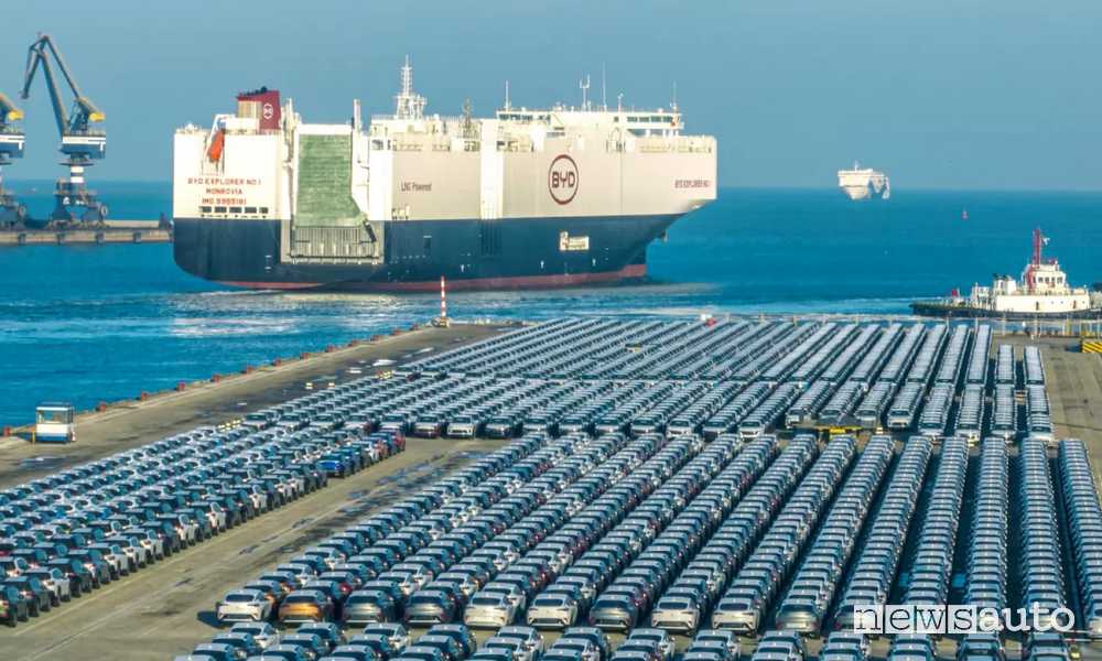 auto elettriche cinesi sulla banchina del porto con nave che trasporta auto.