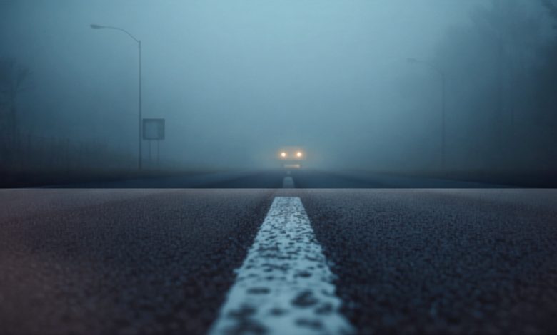 Velocità nella nebbia: fari di un'auto e linea di margine su strada immersa nella nebbia fitta