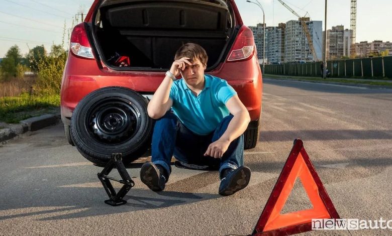 Ruotino di scorta e triangolo di emergenza accanto a un'auto ferma per una foratura